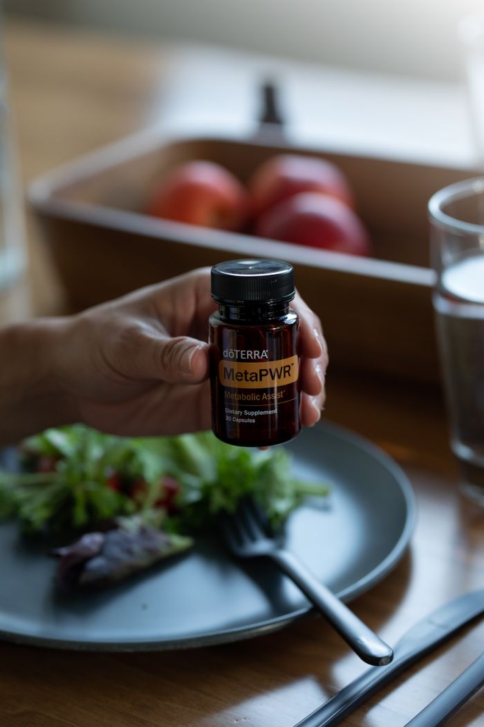 Close-up of a hand holding a dietary supplement bottle over a salad, emphasizing health and wellness.